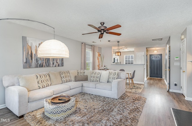 living room with baseboards, wood finished floors, visible vents, and a textured ceiling