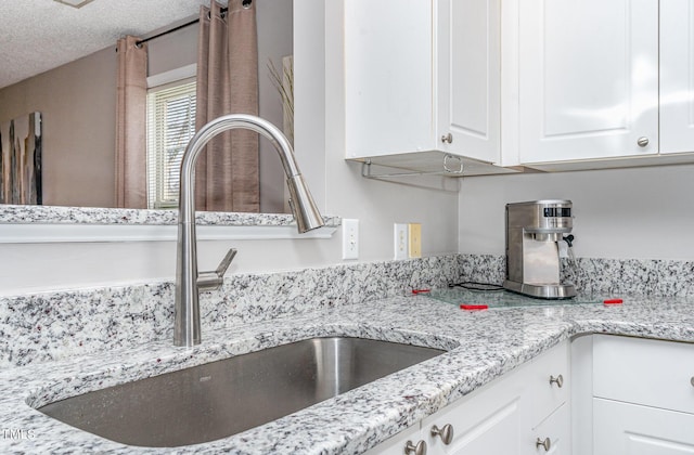 interior details featuring a sink, light stone countertops, a textured ceiling, and white cabinets