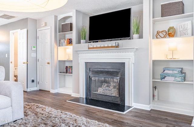 living area with a glass covered fireplace, wood finished floors, baseboards, and a textured ceiling