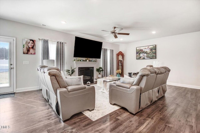 living room with dark wood-style floors, a glass covered fireplace, ceiling fan, and baseboards