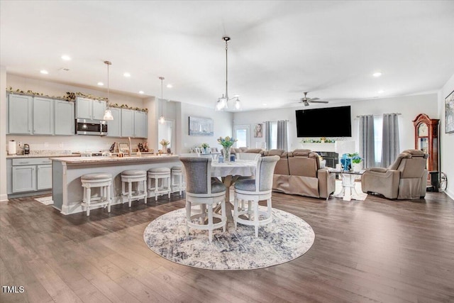 dining space with a ceiling fan, dark wood-type flooring, recessed lighting, and a fireplace