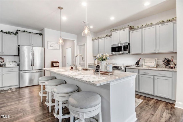 kitchen featuring a breakfast bar area, an island with sink, dark wood-style floors, stainless steel appliances, and a sink