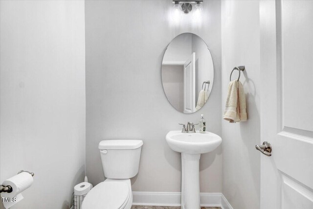 half bath with a sink, baseboards, and toilet