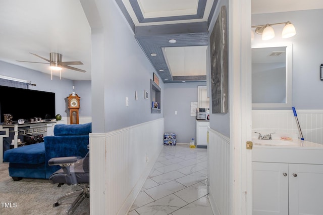 hallway with visible vents, a wainscoted wall, arched walkways, marble finish floor, and a sink