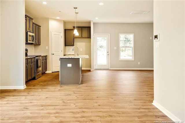 kitchen featuring a center island with sink, tasteful backsplash, light wood-type flooring, and stainless steel appliances