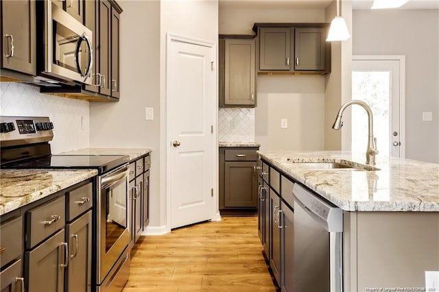 kitchen with light stone counters, light wood-style floors, appliances with stainless steel finishes, and a sink