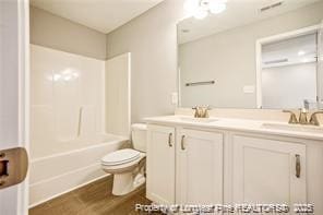 full bath featuring toilet, a sink, wood finished floors, double vanity, and shower / bath combination