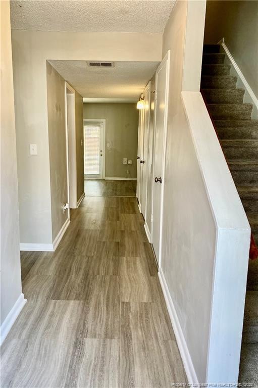 corridor featuring visible vents, a textured ceiling, wood finished floors, baseboards, and stairs