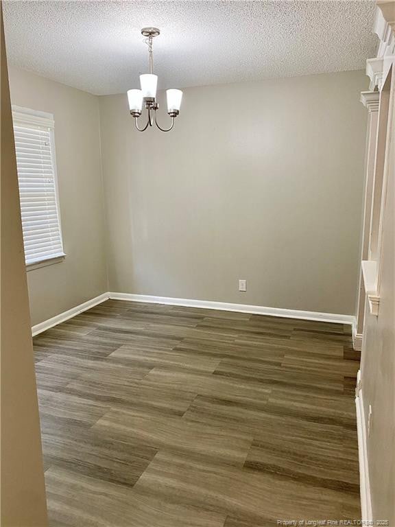 unfurnished room with baseboards, a textured ceiling, a chandelier, and dark wood finished floors