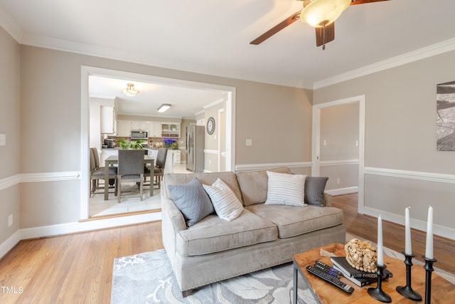 living room featuring a ceiling fan, baseboards, light wood-type flooring, and ornamental molding