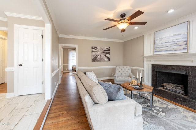 living room with ceiling fan, baseboards, ornamental molding, a fireplace, and light wood-style floors