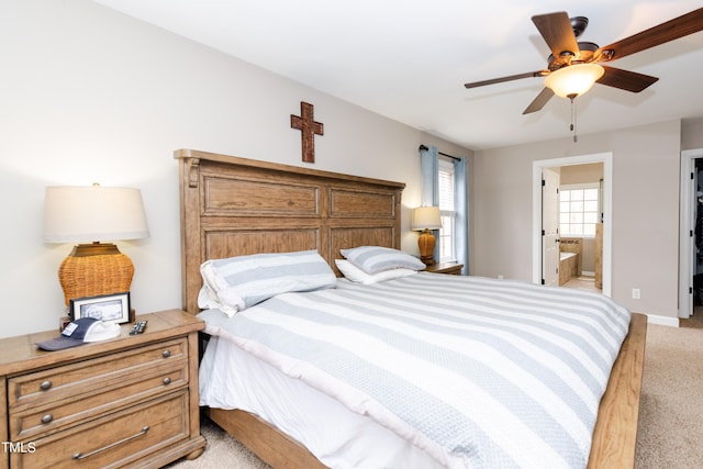 bedroom with connected bathroom, light colored carpet, baseboards, and ceiling fan