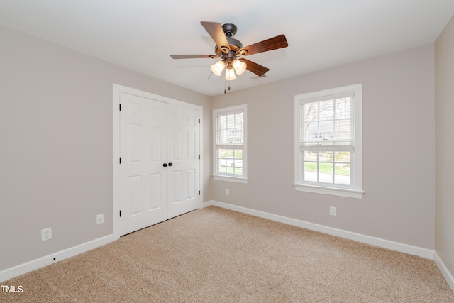 unfurnished bedroom featuring a closet, baseboards, light colored carpet, and a ceiling fan