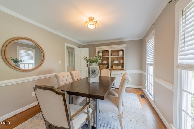 dining area featuring visible vents, baseboards, light wood finished floors, and ornamental molding