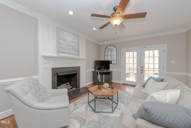 living room featuring french doors, light wood-style floors, ornamental molding, and a fireplace