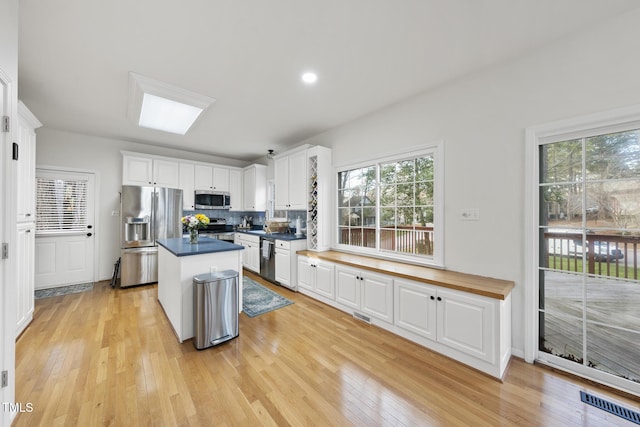 kitchen with light wood-type flooring, backsplash, a center island, white cabinetry, and appliances with stainless steel finishes