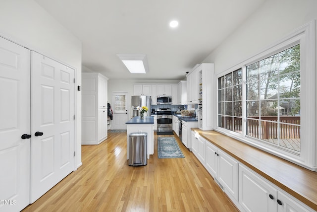 kitchen featuring backsplash, a kitchen island, appliances with stainless steel finishes, light wood-style floors, and white cabinets