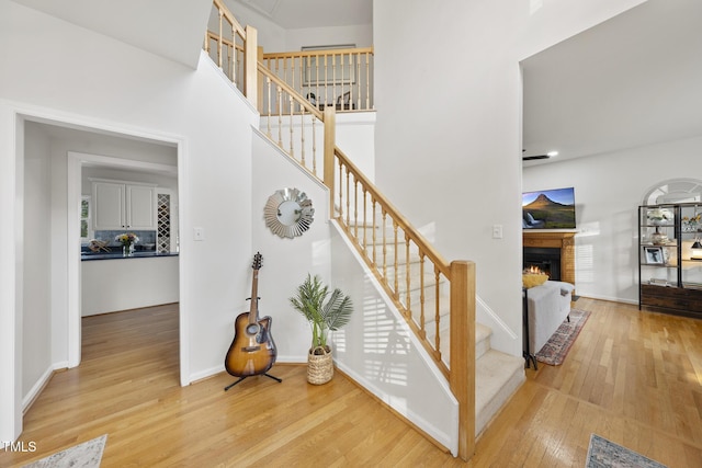 stairway featuring baseboards, a lit fireplace, hardwood / wood-style floors, and a towering ceiling