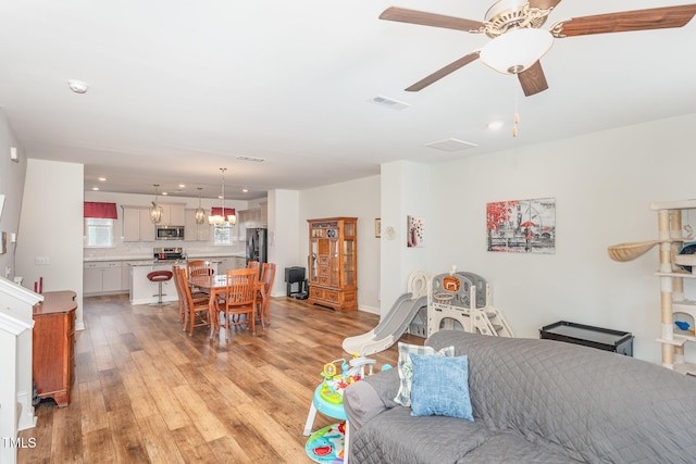 living area featuring visible vents, light wood-style floors, and ceiling fan with notable chandelier