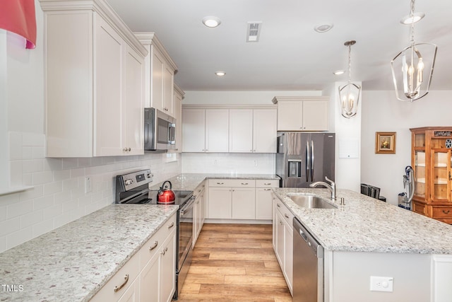 kitchen with a center island with sink, decorative backsplash, light wood-style floors, stainless steel appliances, and a sink