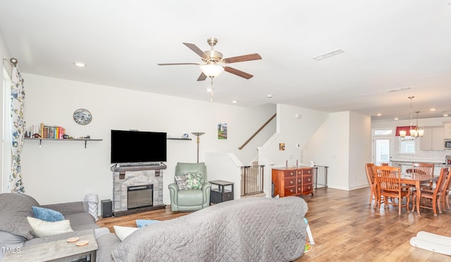 living room with light wood finished floors, stairs, recessed lighting, ceiling fan with notable chandelier, and a fireplace