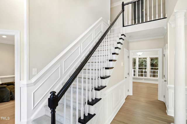 stairs with a decorative wall, wood finished floors, a towering ceiling, and ornamental molding