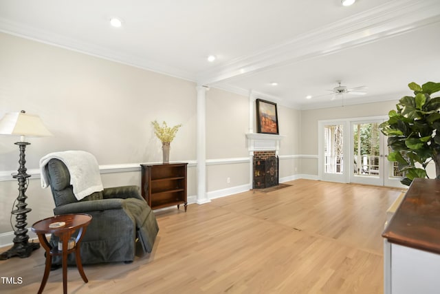 sitting room featuring a fireplace with flush hearth, light wood-style floors, crown molding, baseboards, and ornate columns