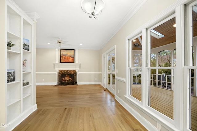 unfurnished living room featuring crown molding, baseboards, ceiling fan, light wood-type flooring, and a fireplace