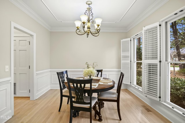 dining room with light wood finished floors, visible vents, crown molding, a wainscoted wall, and an inviting chandelier