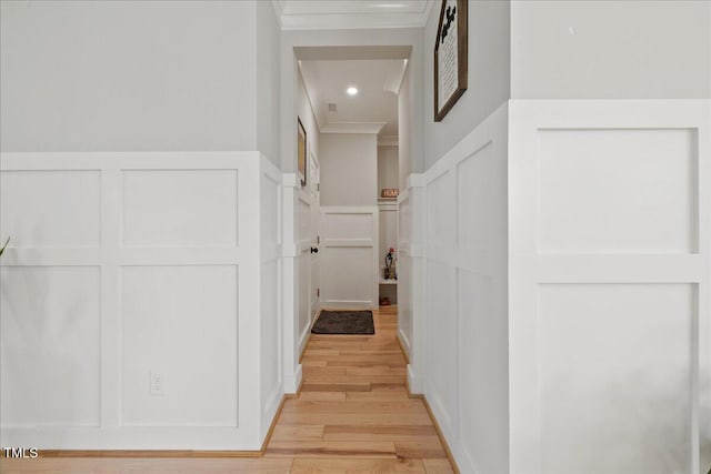 hallway featuring light wood-style flooring, recessed lighting, ornamental molding, wainscoting, and a decorative wall