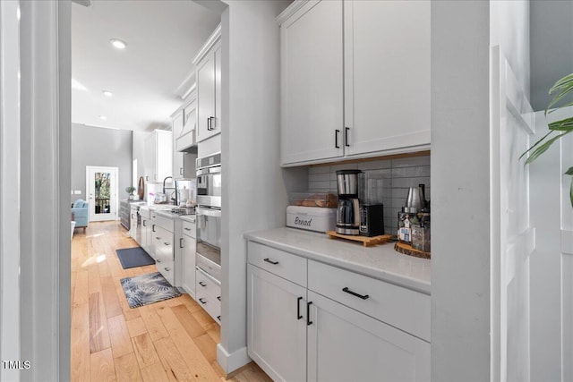 kitchen with oven, light wood-type flooring, backsplash, and white cabinetry