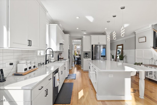 kitchen with a center island, ornamental molding, wainscoting, stainless steel appliances, and white cabinetry