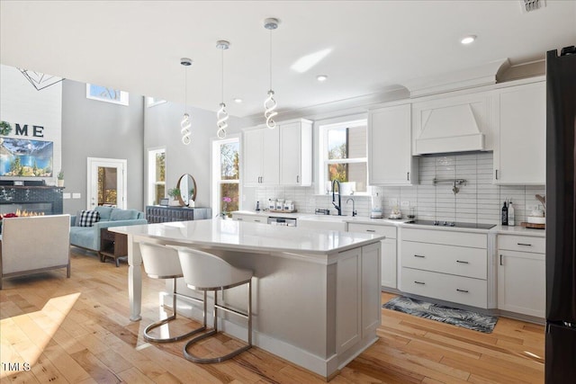 kitchen featuring premium range hood, a breakfast bar area, light wood-type flooring, decorative backsplash, and white cabinetry