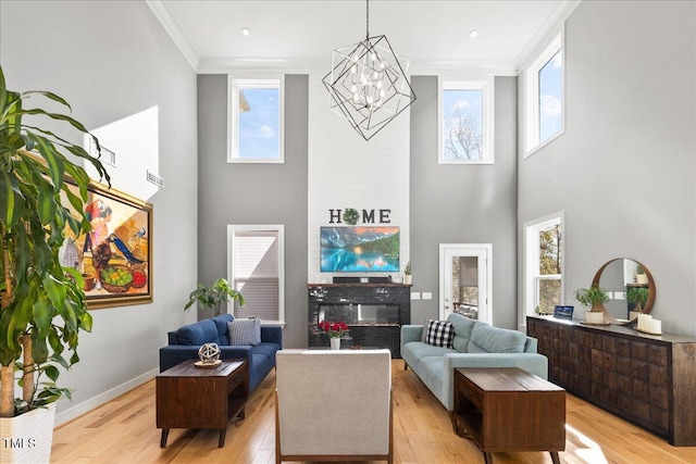 living room featuring light wood-type flooring, a high ceiling, a fireplace, crown molding, and baseboards