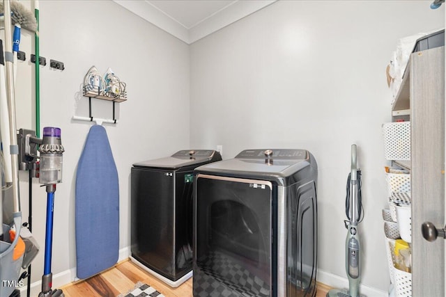 clothes washing area featuring washer and dryer, wood finished floors, crown molding, baseboards, and laundry area