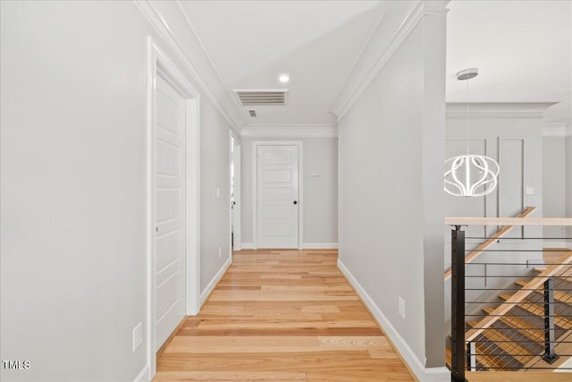 hallway featuring visible vents, ornamental molding, light wood-style floors, an upstairs landing, and a chandelier