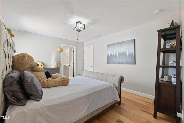 bedroom featuring light wood finished floors, crown molding, ensuite bathroom, and baseboards