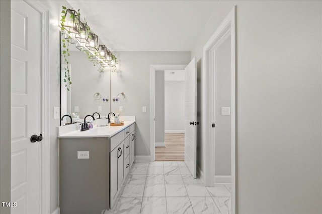 bathroom with double vanity, baseboards, marble finish floor, and a sink