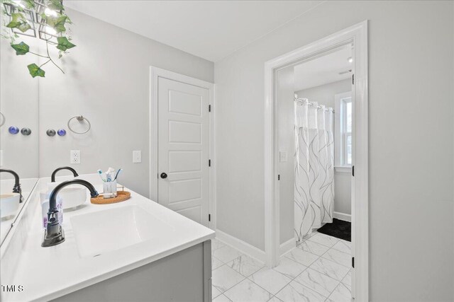 bathroom featuring double vanity, baseboards, marble finish floor, and a sink