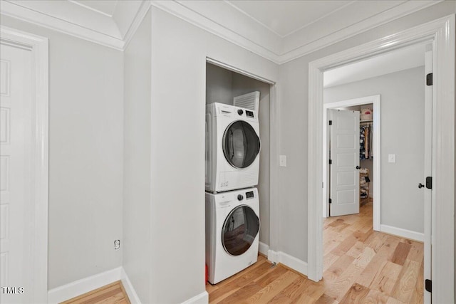 clothes washing area with light wood-style floors, crown molding, laundry area, and stacked washing maching and dryer