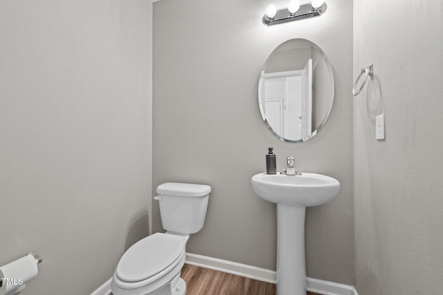 half bath featuring a sink, toilet, baseboards, and wood finished floors