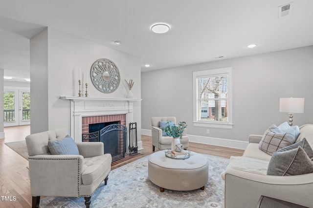 living room with visible vents, a brick fireplace, baseboards, and wood finished floors