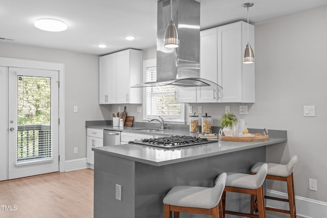 kitchen with a peninsula, wall chimney range hood, a healthy amount of sunlight, and a sink