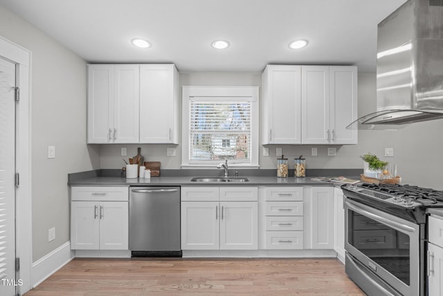 kitchen with dark countertops, wall chimney range hood, appliances with stainless steel finishes, and a sink