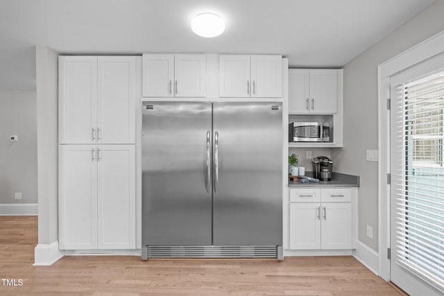 kitchen with light wood-type flooring, stainless steel appliances, baseboards, and white cabinets