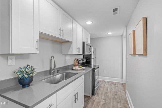 kitchen featuring visible vents, a sink, stainless steel appliances, white cabinets, and light wood finished floors