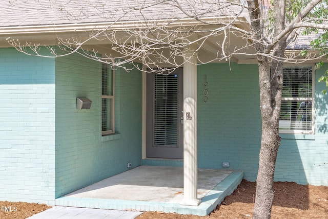 view of exterior entry with brick siding and a shingled roof