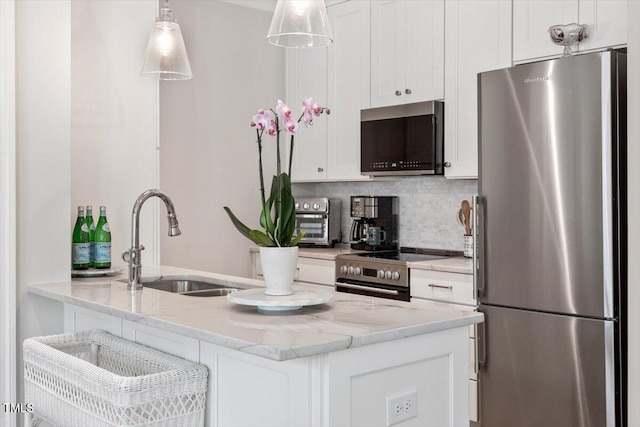 kitchen with light stone counters, appliances with stainless steel finishes, hanging light fixtures, white cabinetry, and a sink