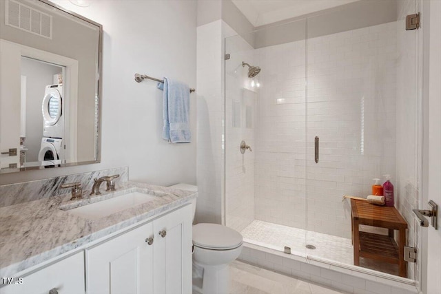 bathroom featuring visible vents, a shower stall, stacked washer / dryer, toilet, and vanity