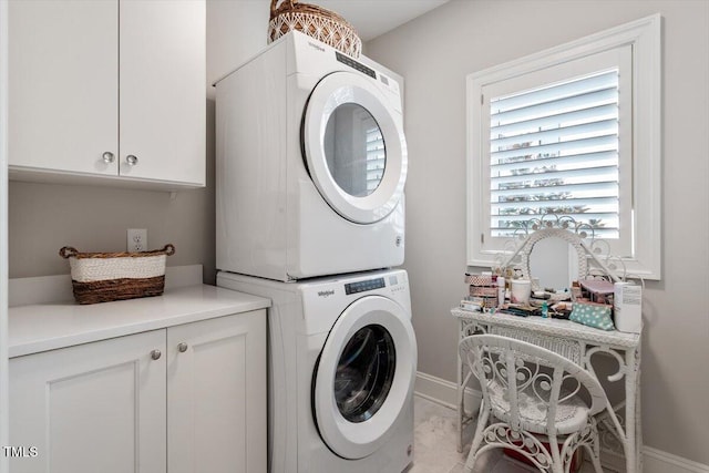 clothes washing area featuring stacked washer / drying machine, cabinet space, and baseboards